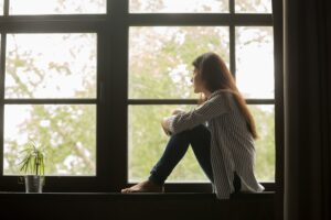 young woman with silent depression sits alone looking out a window